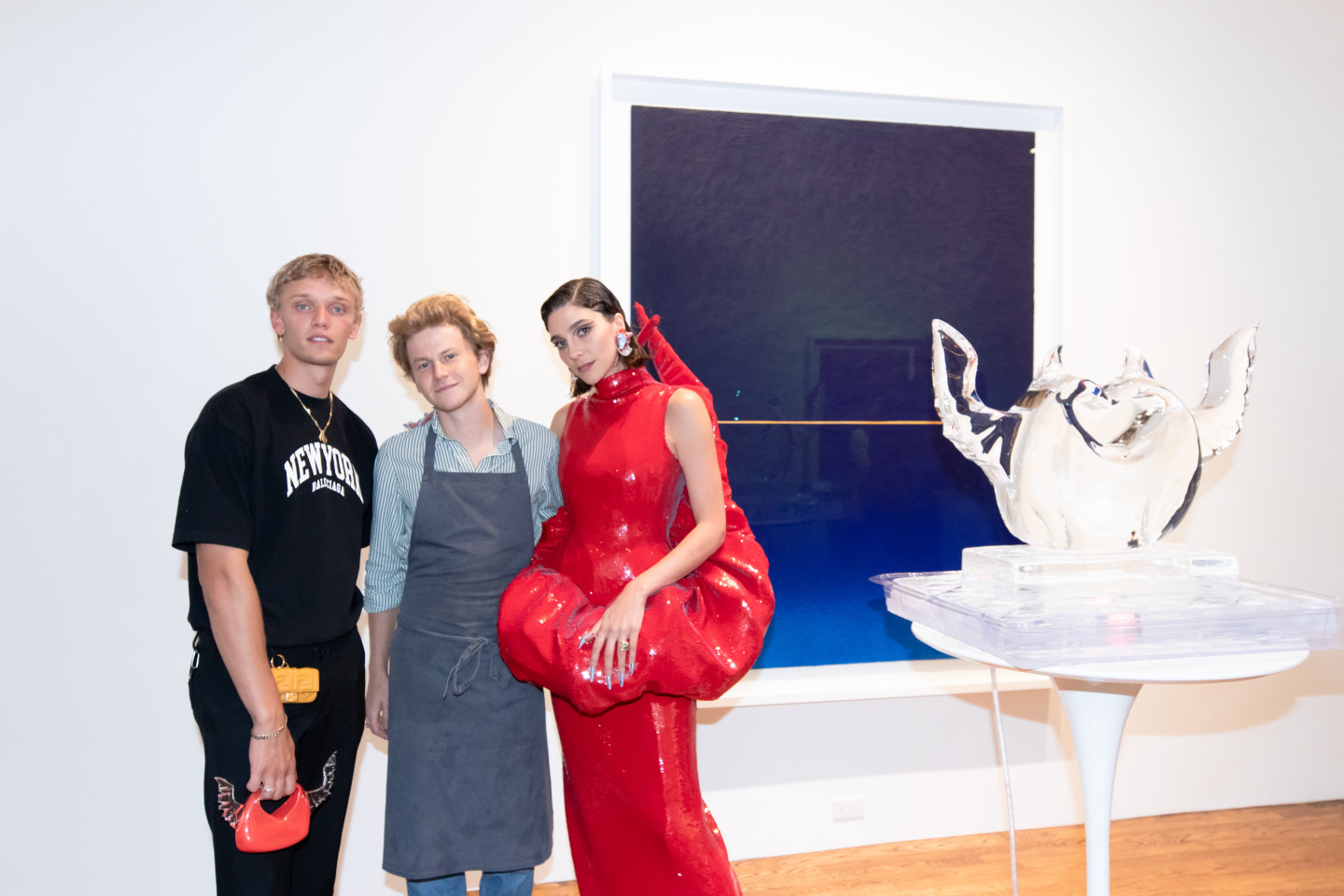 Two men and a woman standing in front of a painting and ice sculpture.