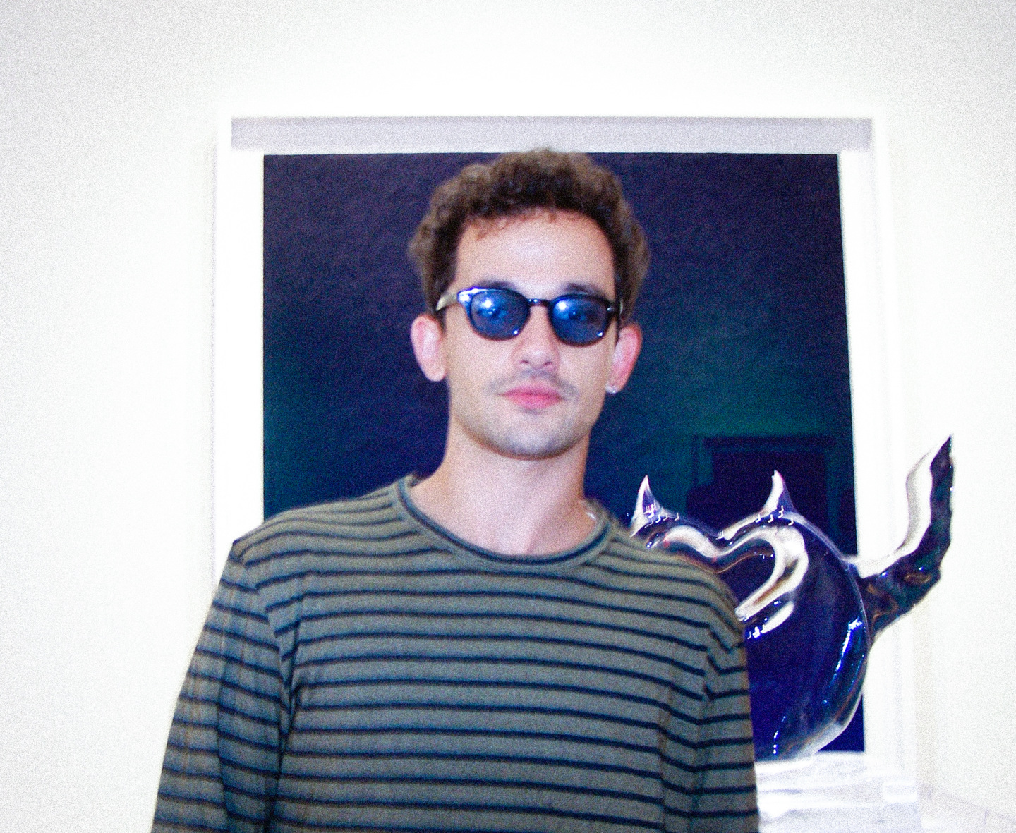 Man in sunglasses standing in front of a painting and ice sculpture.