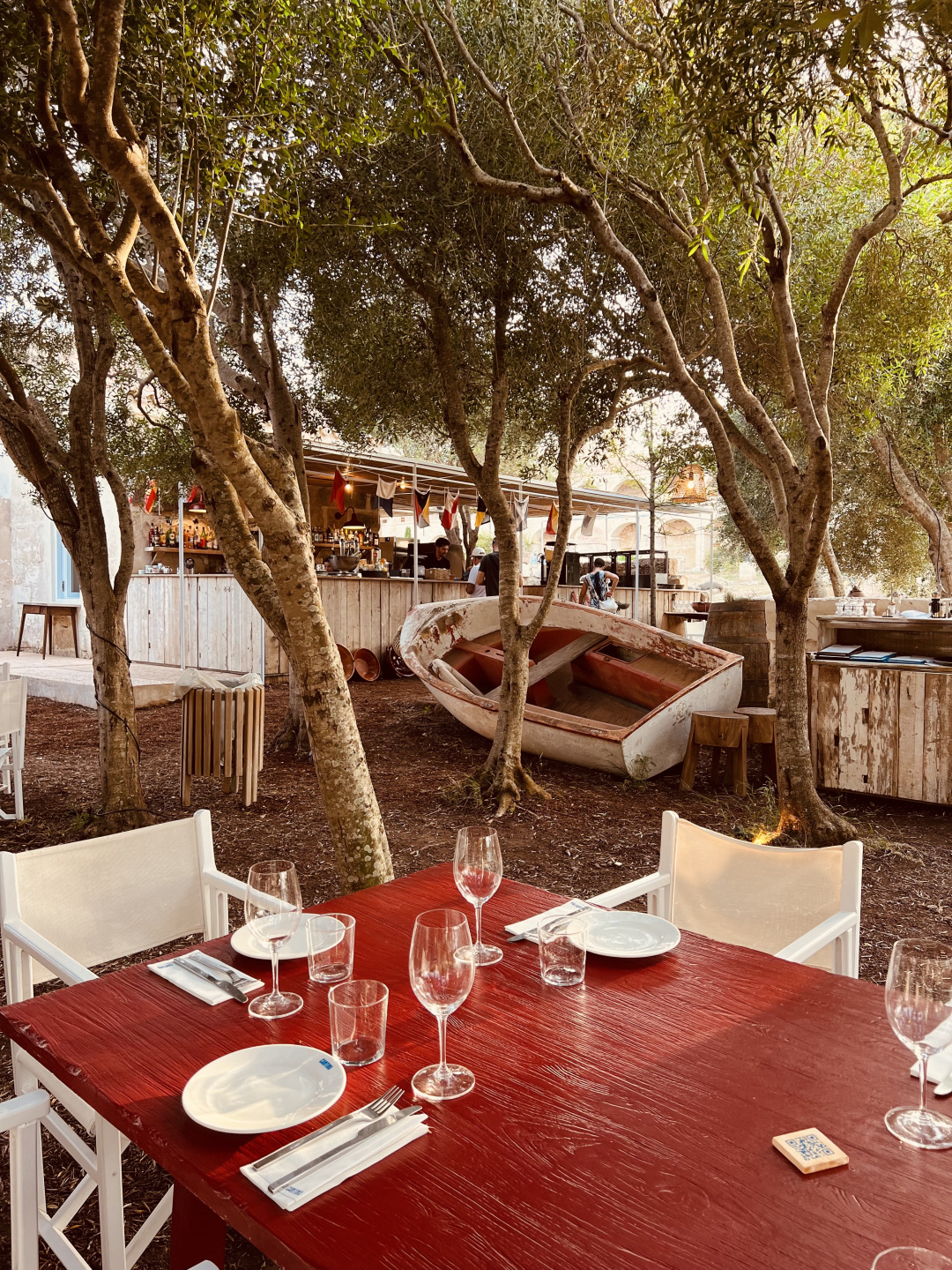 Outdoor restaurant with red tables and boats in background.
