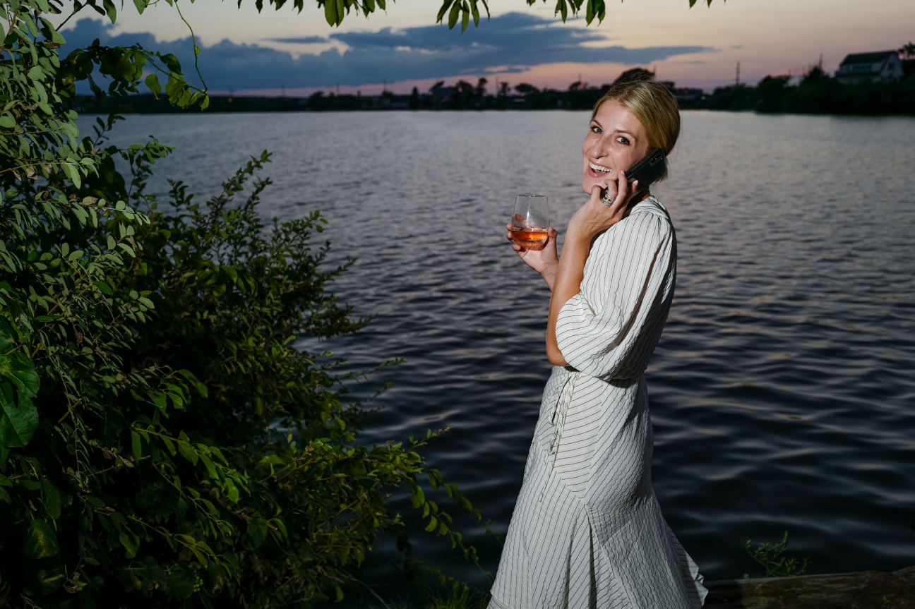 Woman with wine glass stands in front of body of water