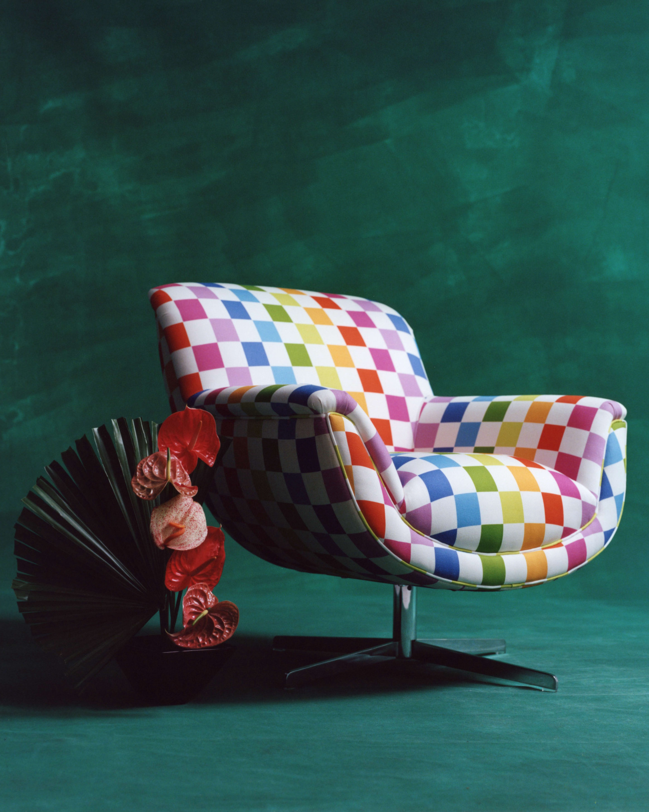 Multicolored checkered chair and a flower arrangement against a dark green backdrop.