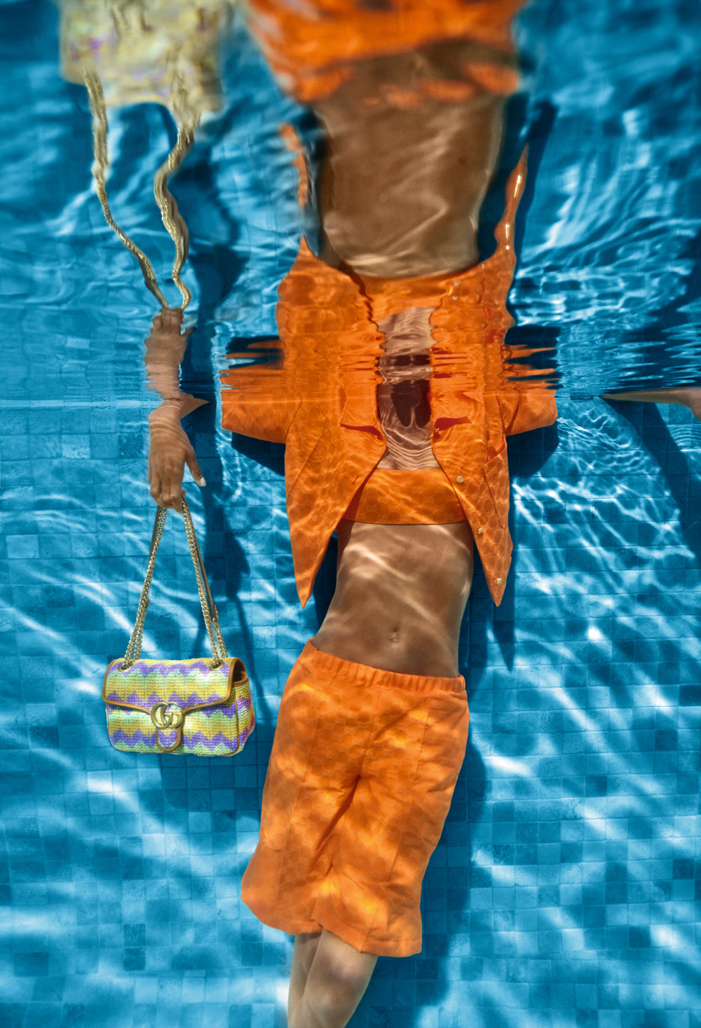 A woman in an orange short and top, holding a bag, underwater.