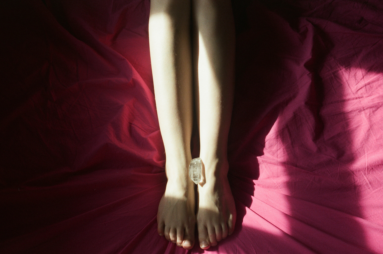a photoof a piece of crystal is placed between a woman’s feet who is in bed on red bedsheets from Lina Scheynius photo-essay for Tabayer jewelry Tabayer jewellery