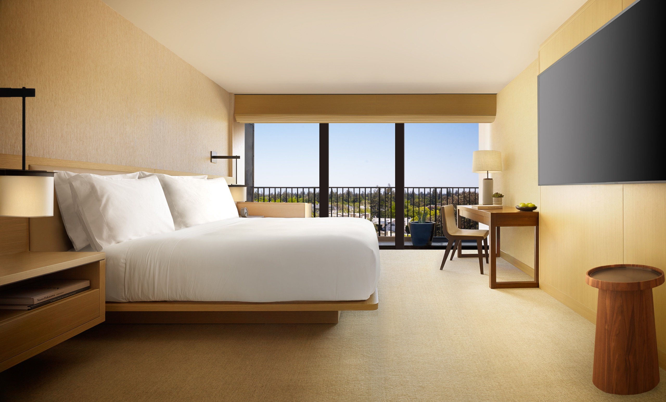 King bed in a modern bedroom with a view of greenery outside the windows.